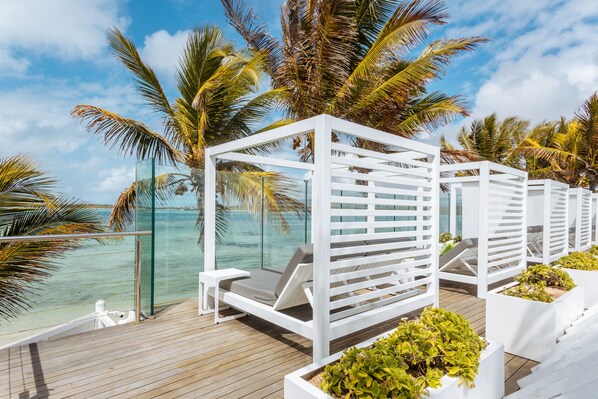A deck with white lounge chairs and planters, overlooking a clear blue sea with palm trees. - Tropical Attitude - Adults only (Trou d'Eau Douce)