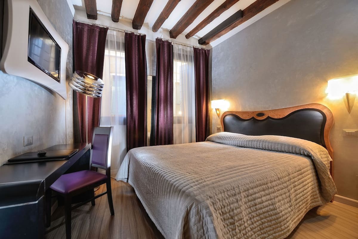 A hotel room with a bed, desk, chair, and curtains.