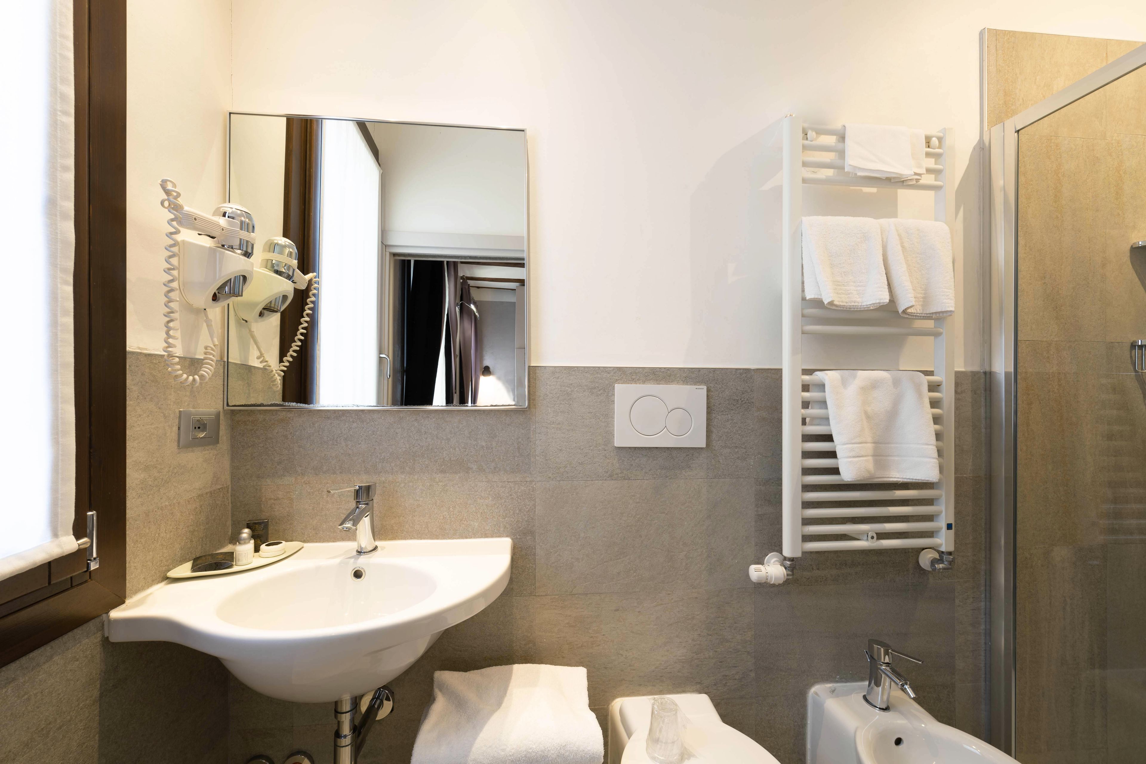 Un bagno con lavandino, specchio, asciugacapelli, portasciuga e zona doccia.