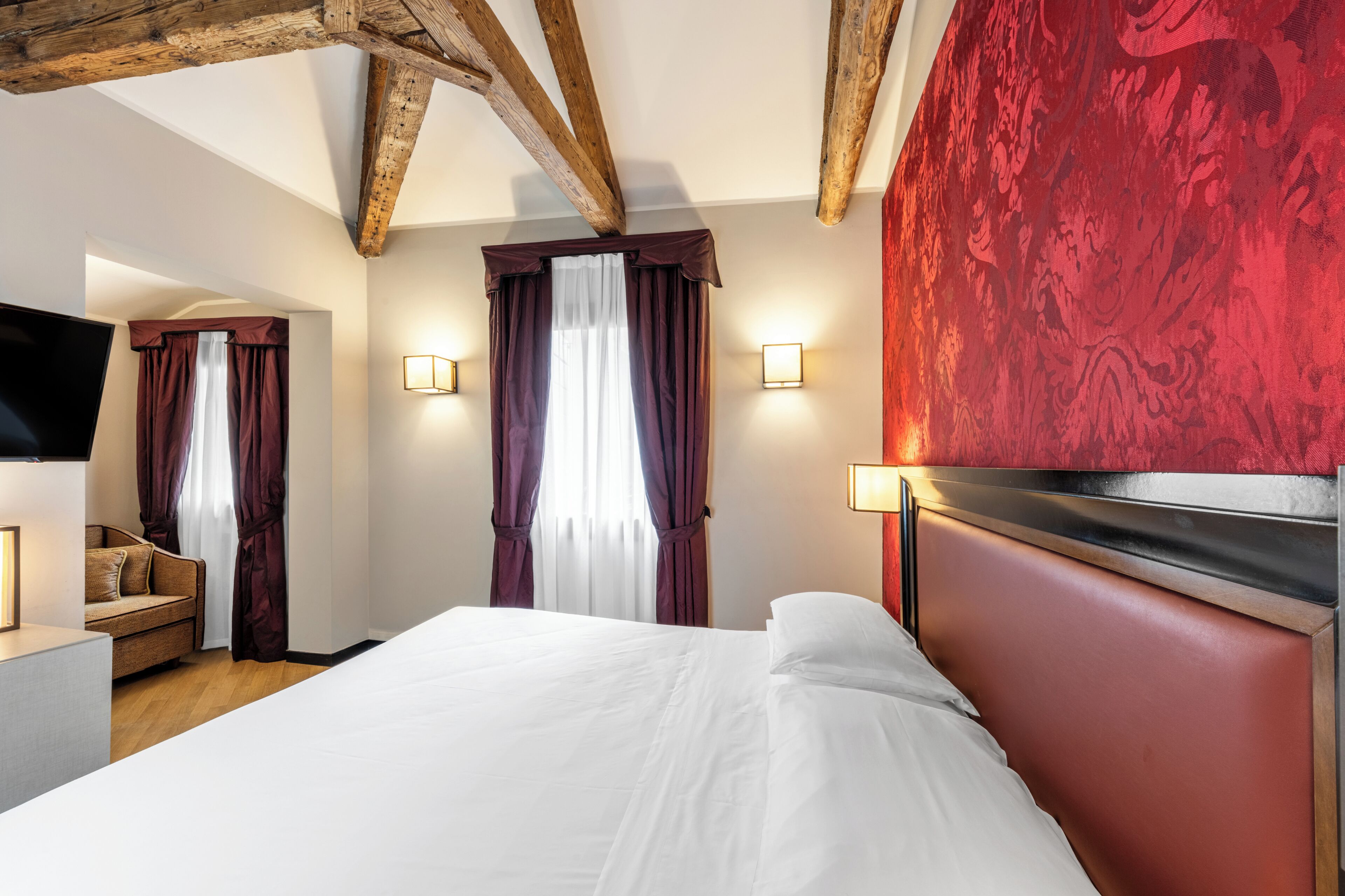 Une chambre d’hôtel avec un lit, une télévision, un canapé et une fenêtre avec des rideaux.