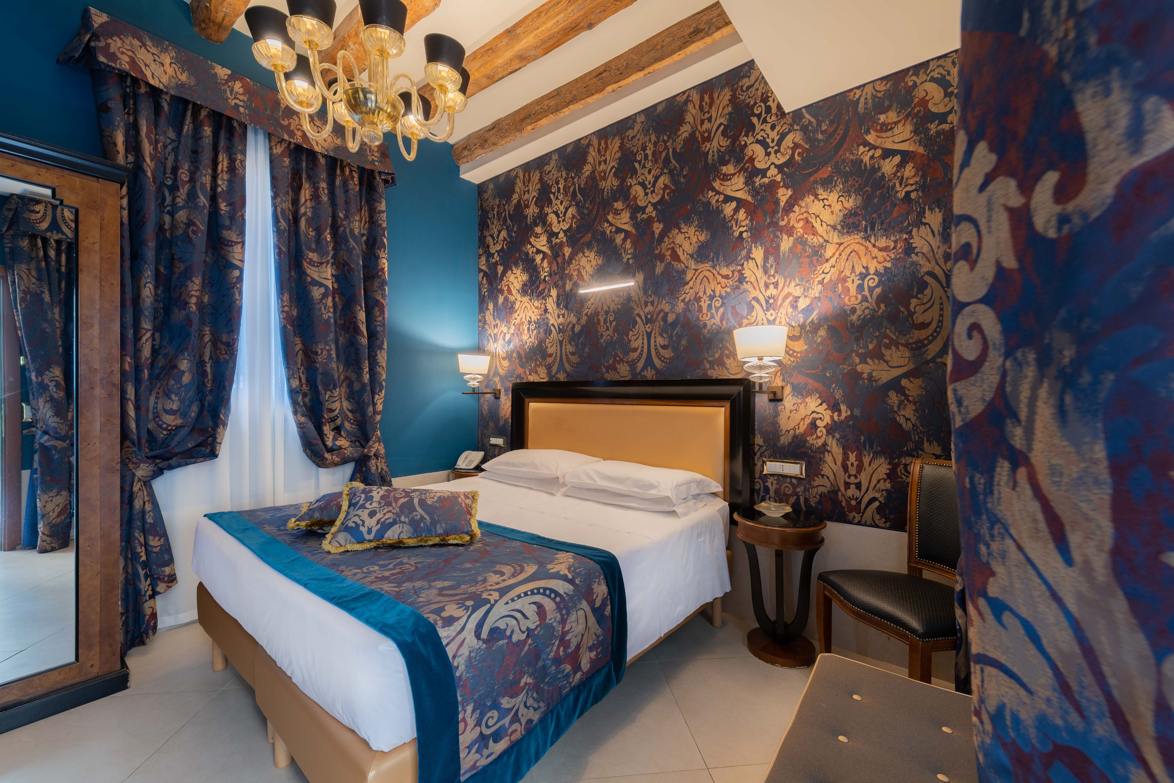 A hotel room with a large bed, a wooden headboard, a bedside table with a lamp, and a chair.