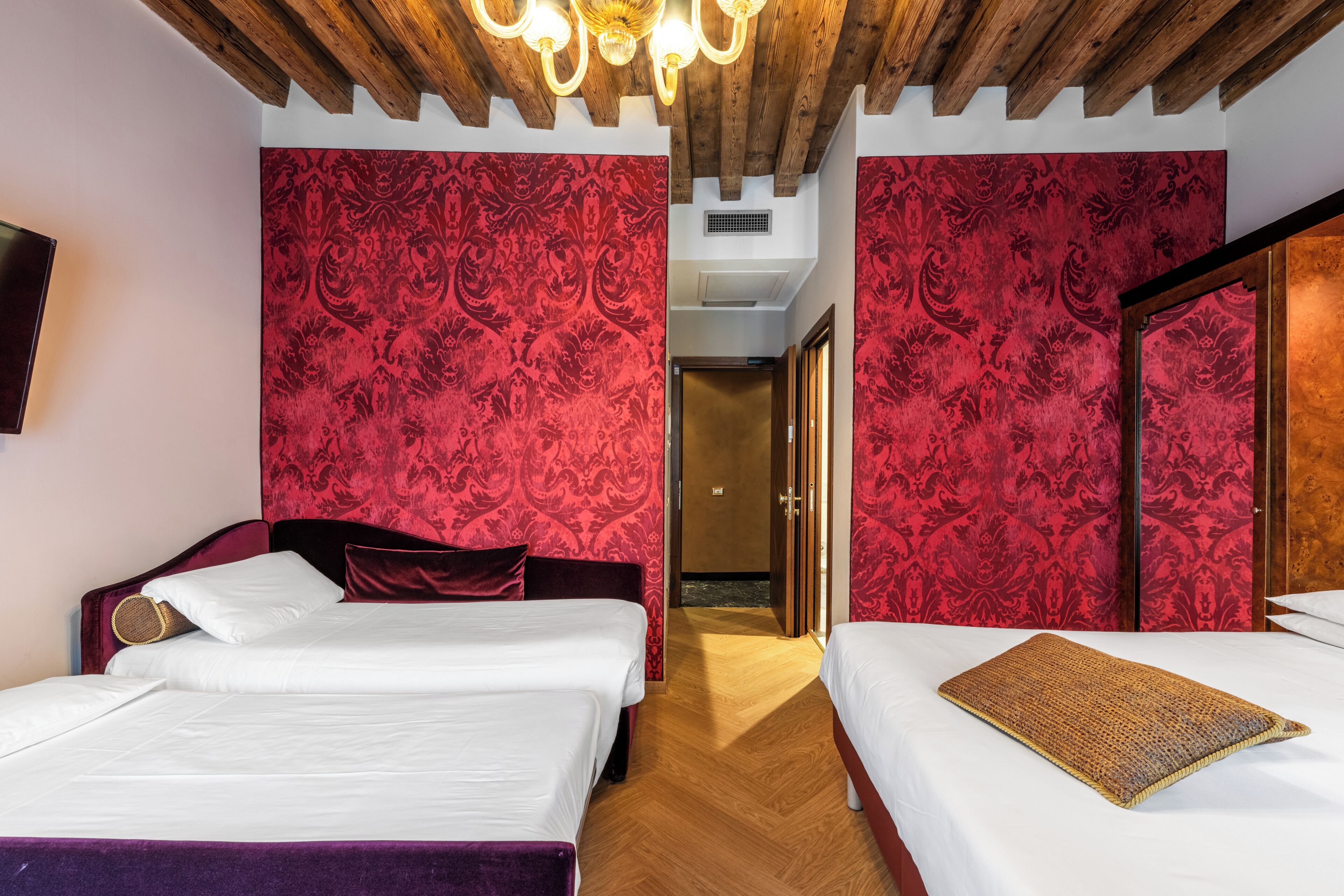 Habitación de hotel con dos camas, techo de madera y papel tapiz rojo estampado.