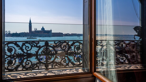 A view from a window with ornate iron railings overlooking a body of water with buildings in the background. - Hotel Paganelli (Venice)