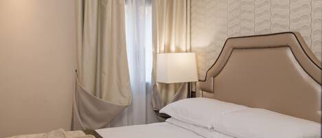 A hotel room with a bed, a bedside lamp, and a window with curtains.
