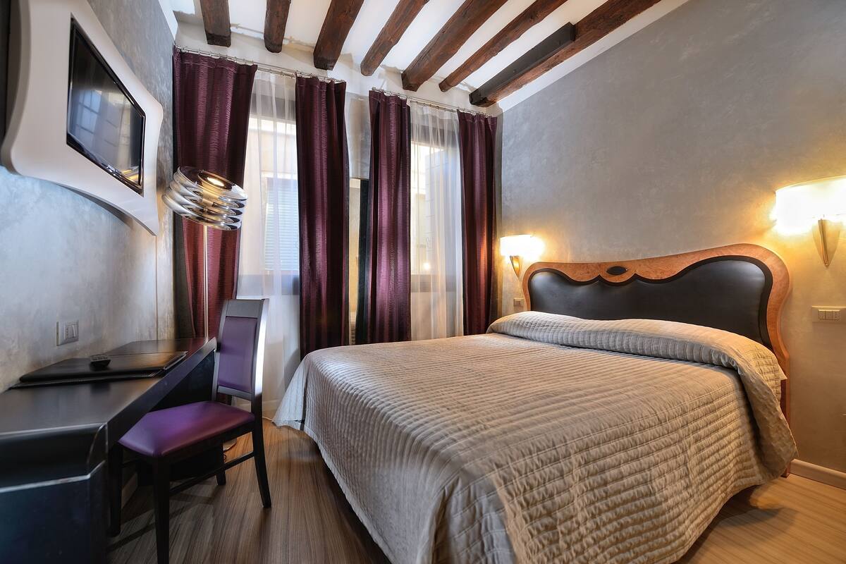 A hotel room with a bed, a desk, a chair, and a TV mounted on the wall.
