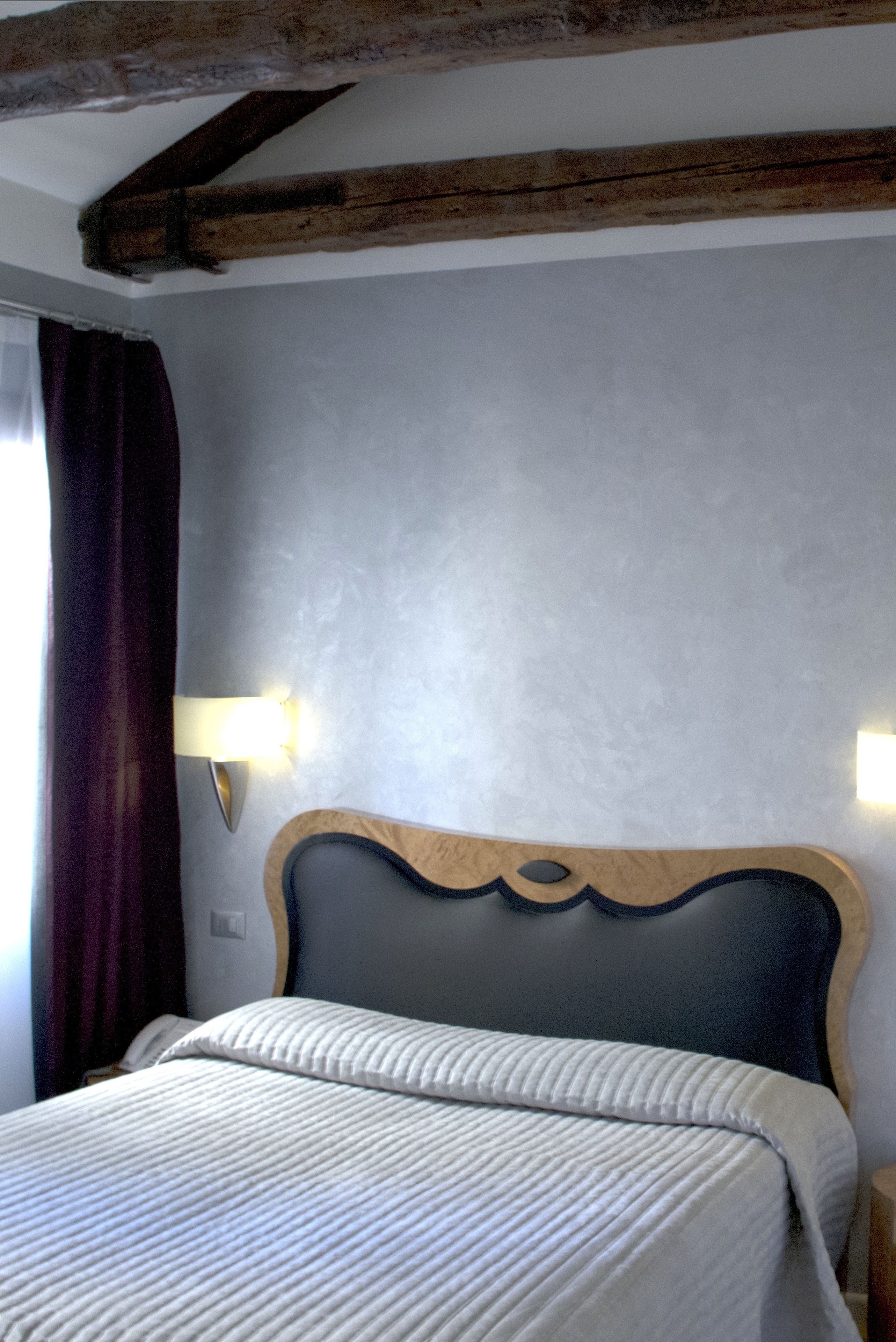 Une chambre à coucher avec une tête de lit en bois, un lit recouvert d’une couvre-lit à rayures et deux appliques murales.
