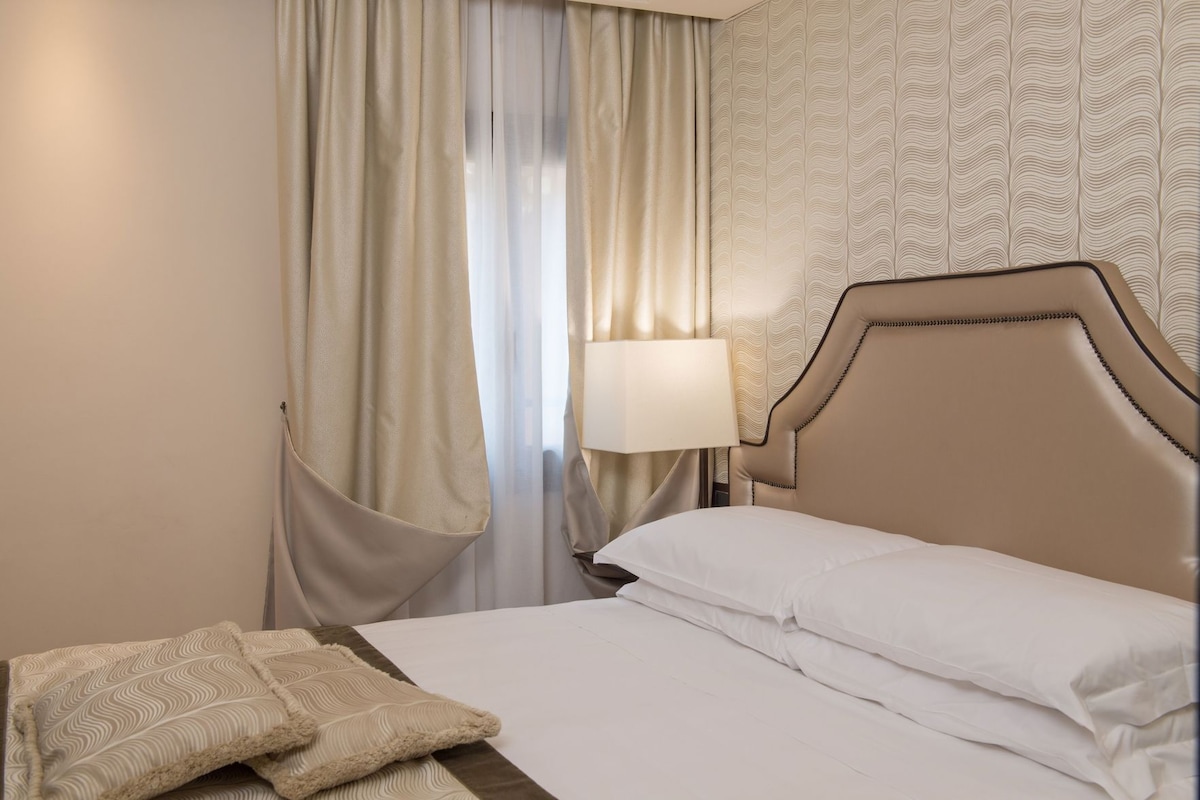 A hotel room with a bed, a nightstand, a lamp, and a window with curtains.