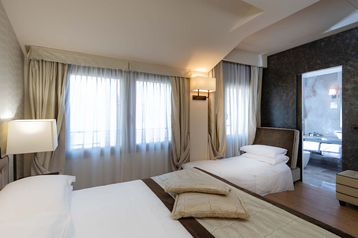 A hotel room with two beds, a sitting area, and a view of the outside.