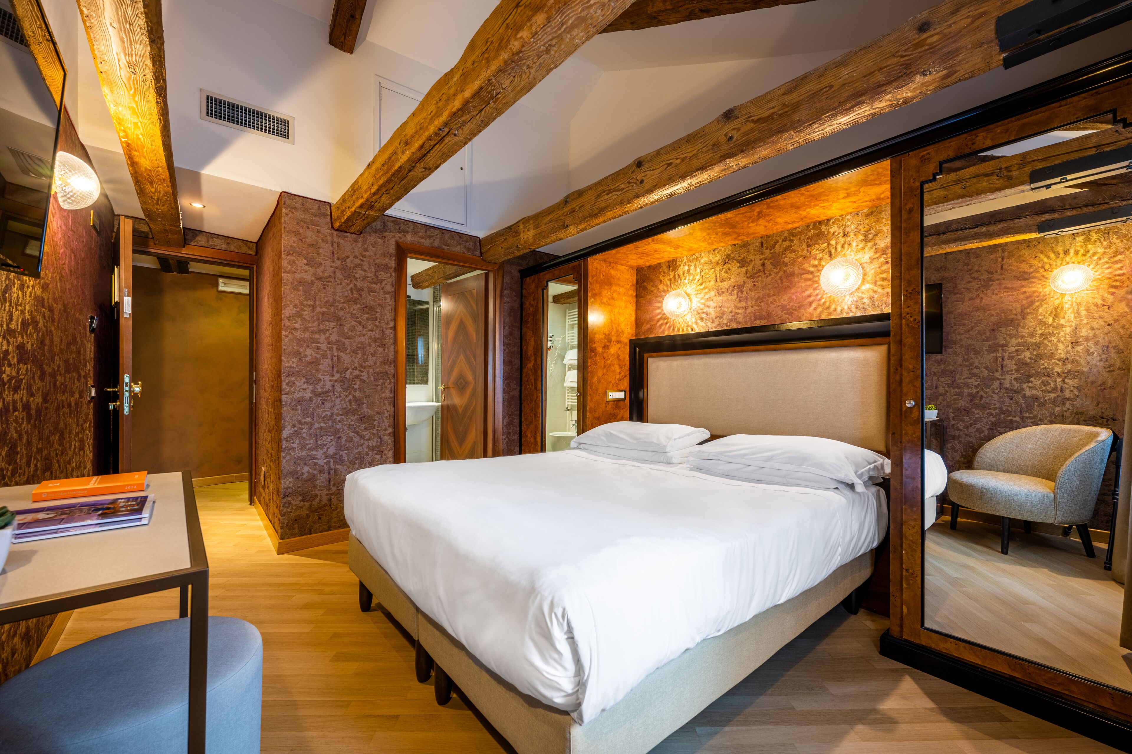 A bedroom with a large bed, a desk with a chair, and a mirror.