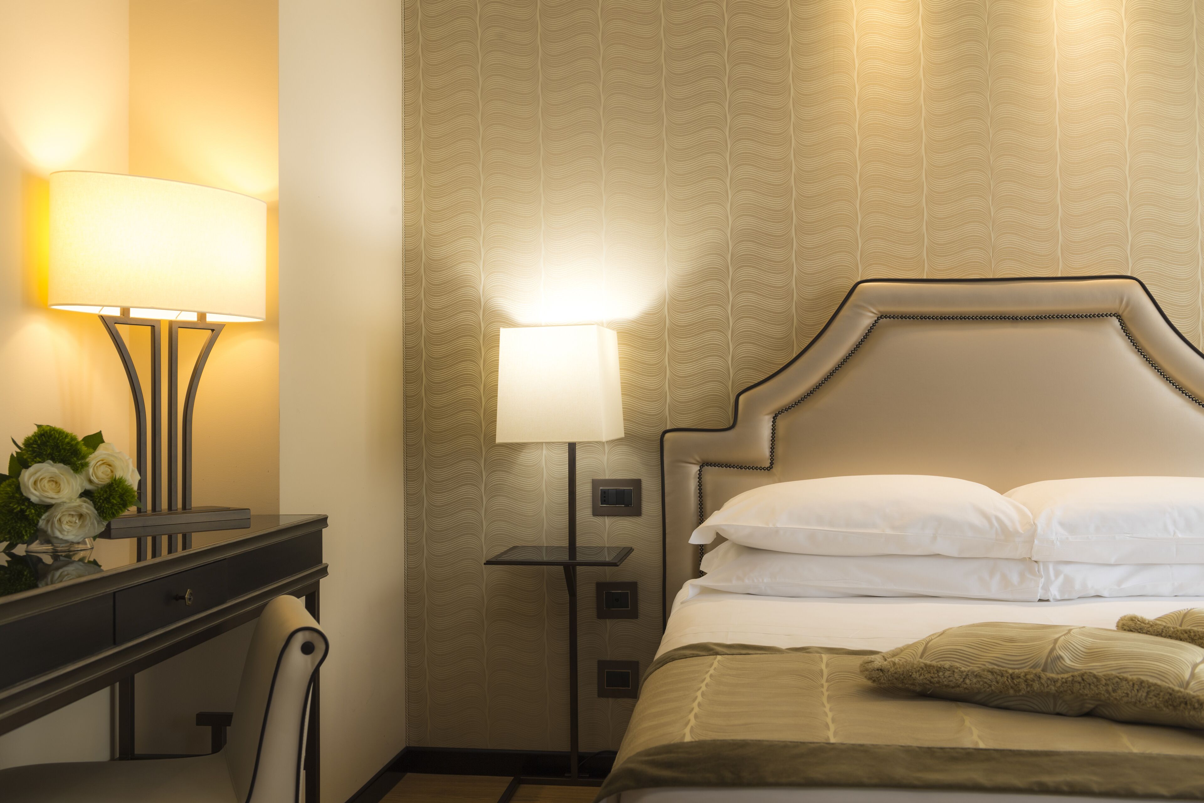 A hotel room with a bed, a desk with a lamp, and a nightstand with a lamp.