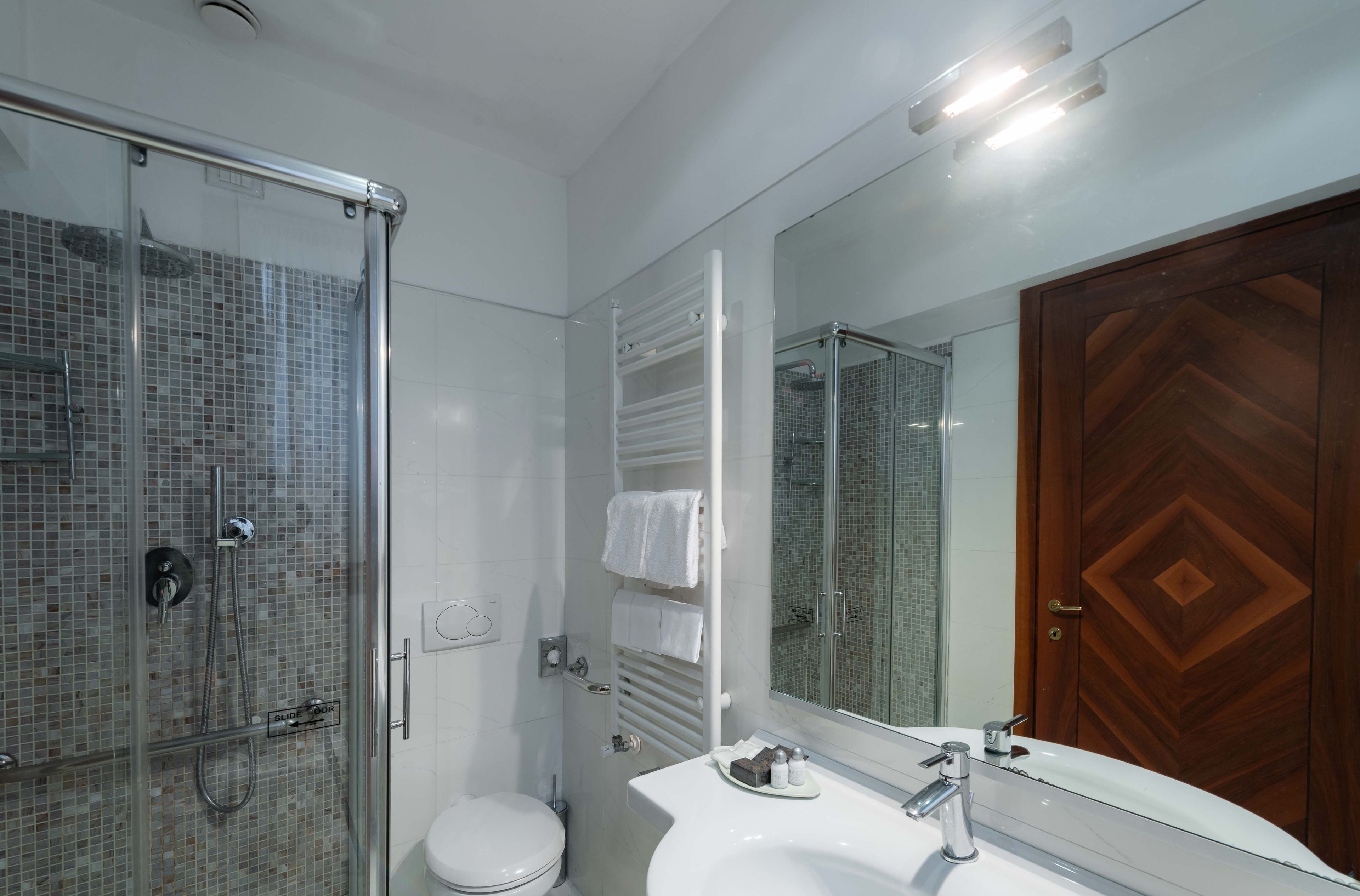 A modern bathroom with a glass-enclosed shower, a white toilet, and a large mirror with a wooden door.