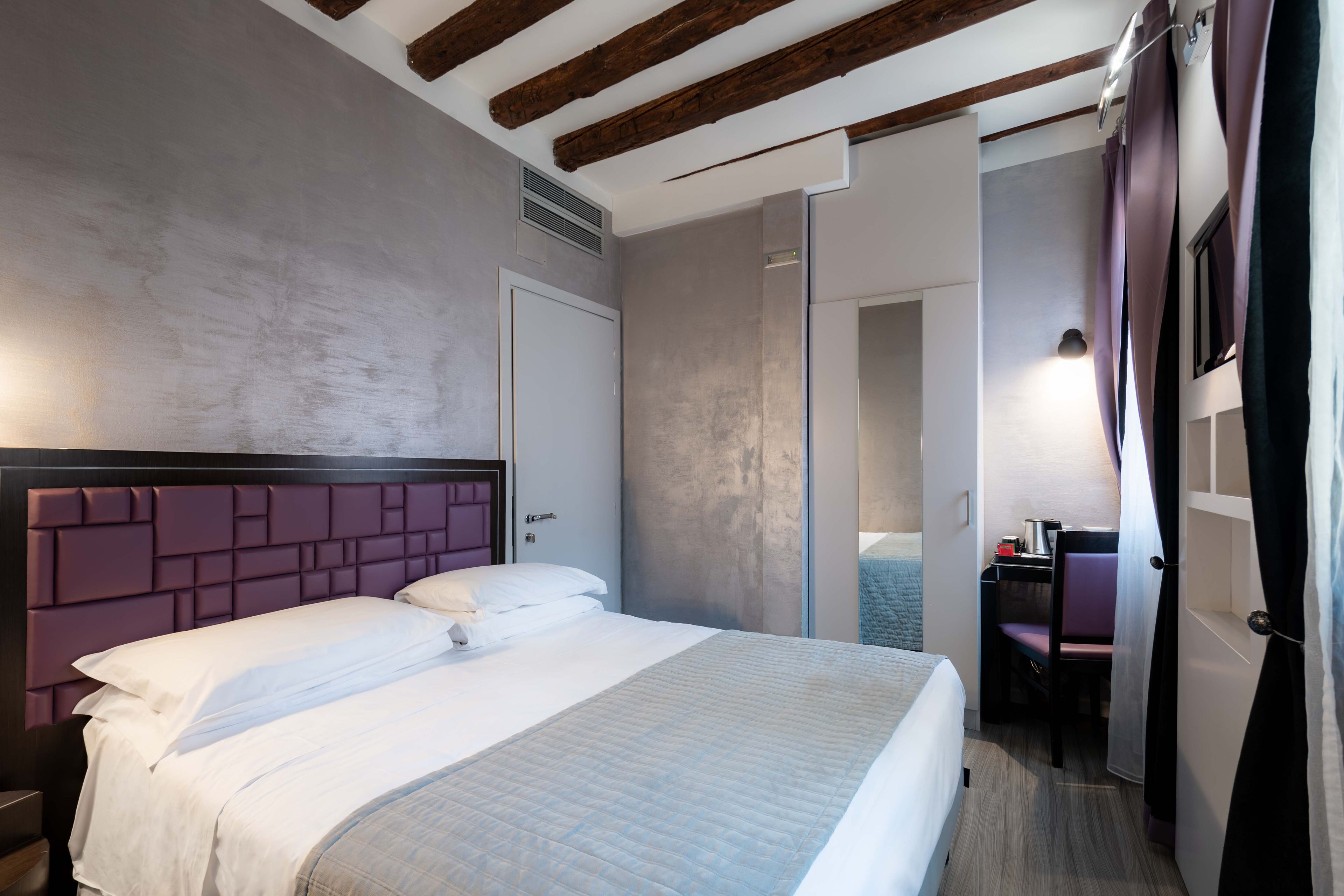 A modern hotel room with a large bed, a wooden ceiling, and a desk with a chair.