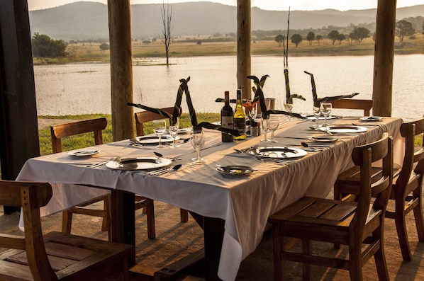 A dining table set for a meal with a view of a lake and hills in the background.