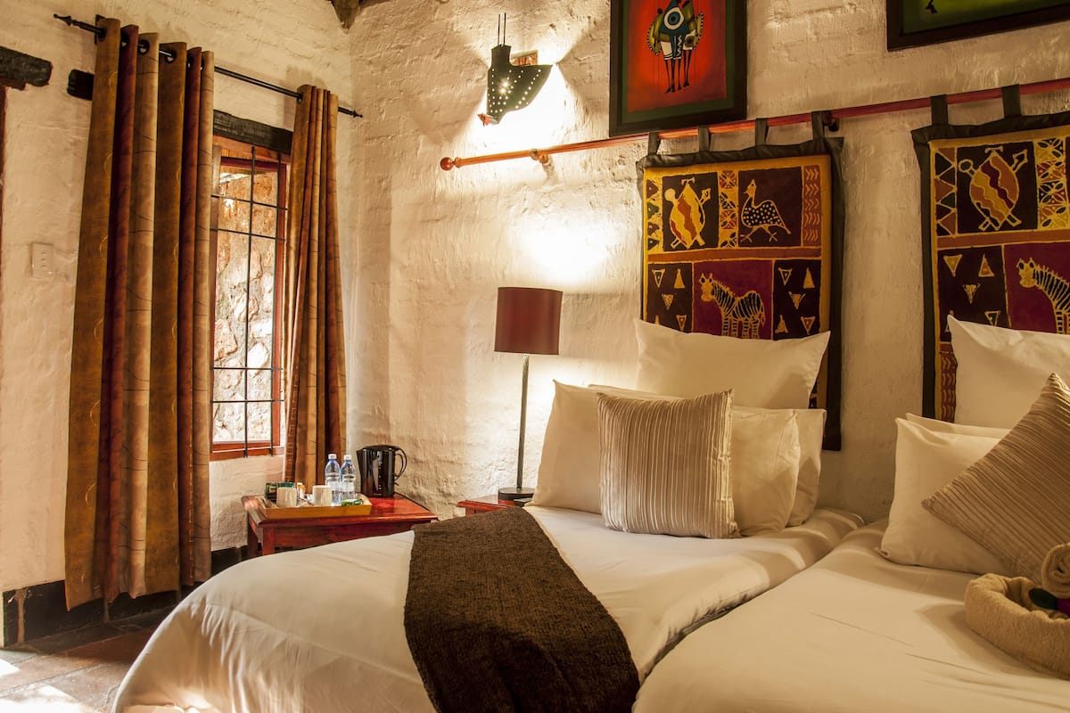 Habitación de hotel con una cama, una mesita de noche, una lámpara y una ventana con cortinas.