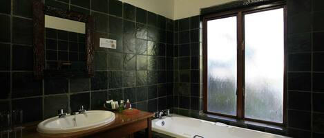 A bathroom with dark tiles, a wooden vanity with a sink, a mirror, and a bathtub.