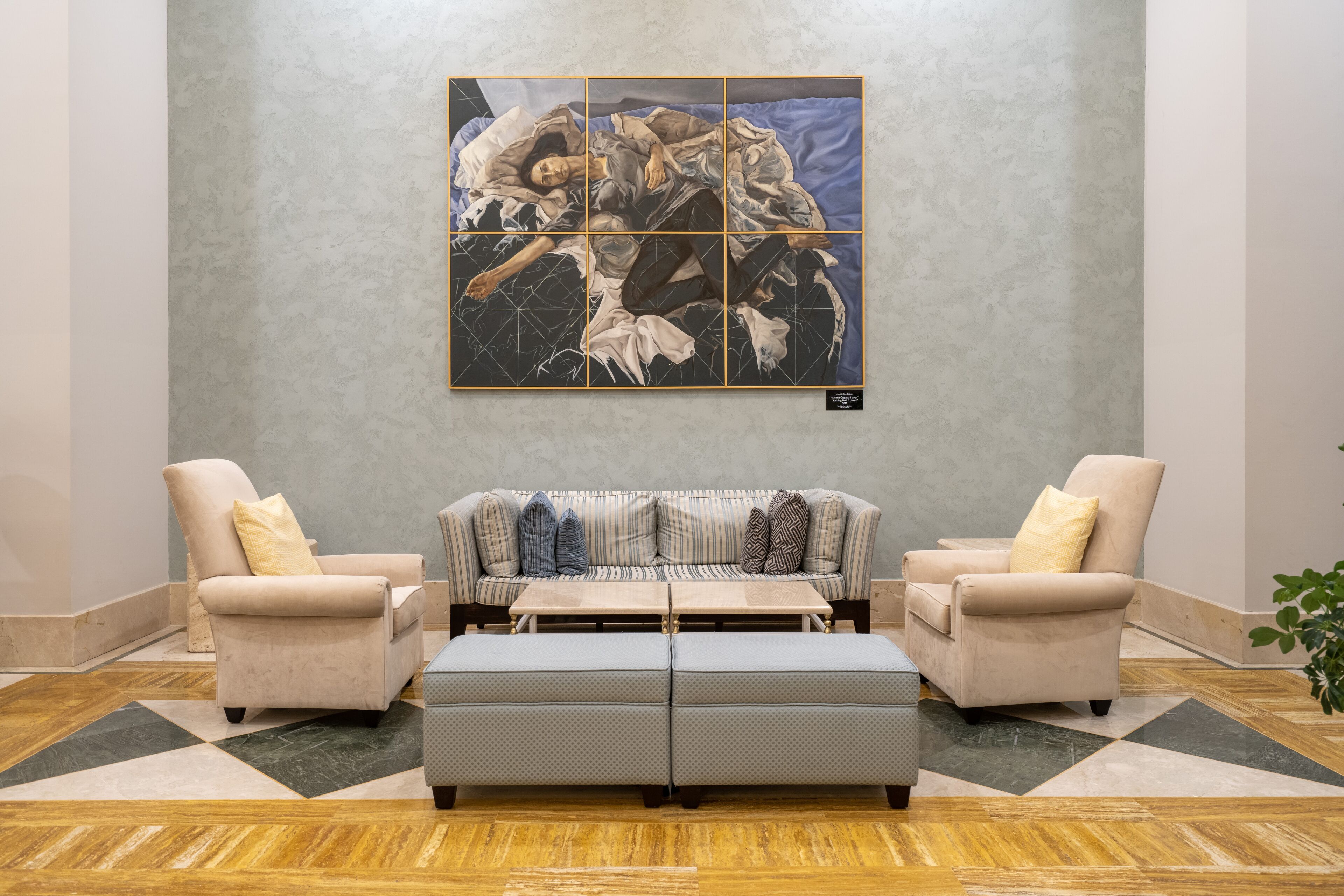 A living room with a sofa, two armchairs, a coffee table, and a large abstract painting on the wall.