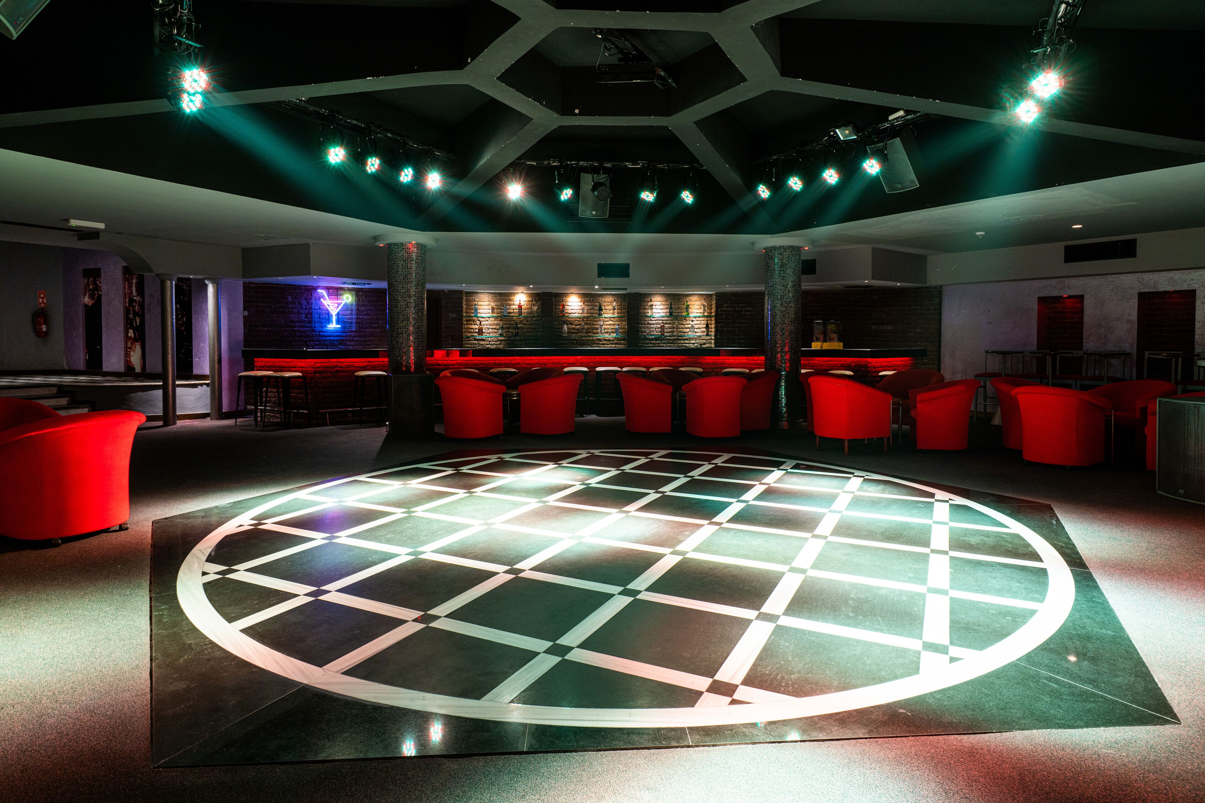 Un bar moderno con una pista de baile circular, asientos rojos y un fondo de pared de ladrillo.