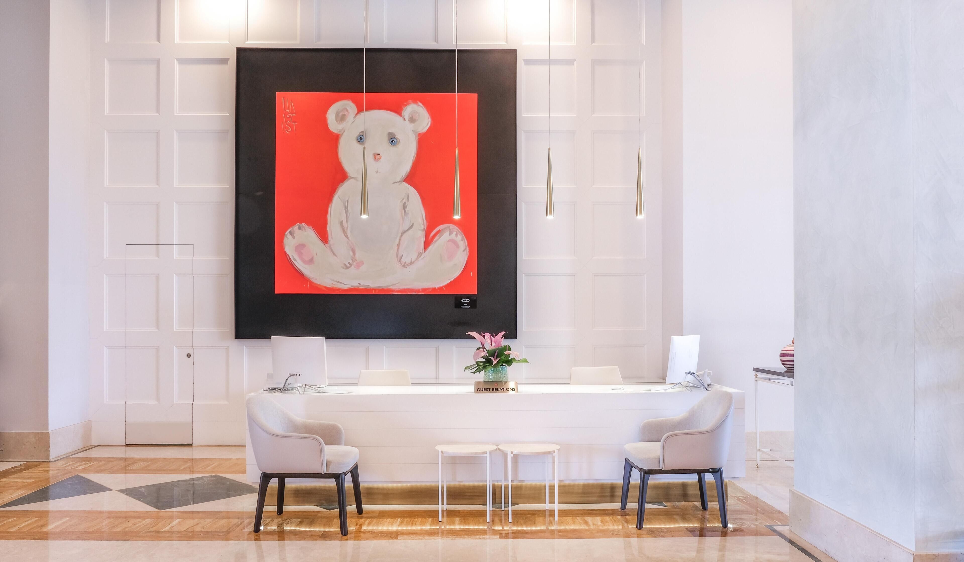 A modern reception area with a large abstract painting, a reception desk, two chairs, and a vase with flowers.