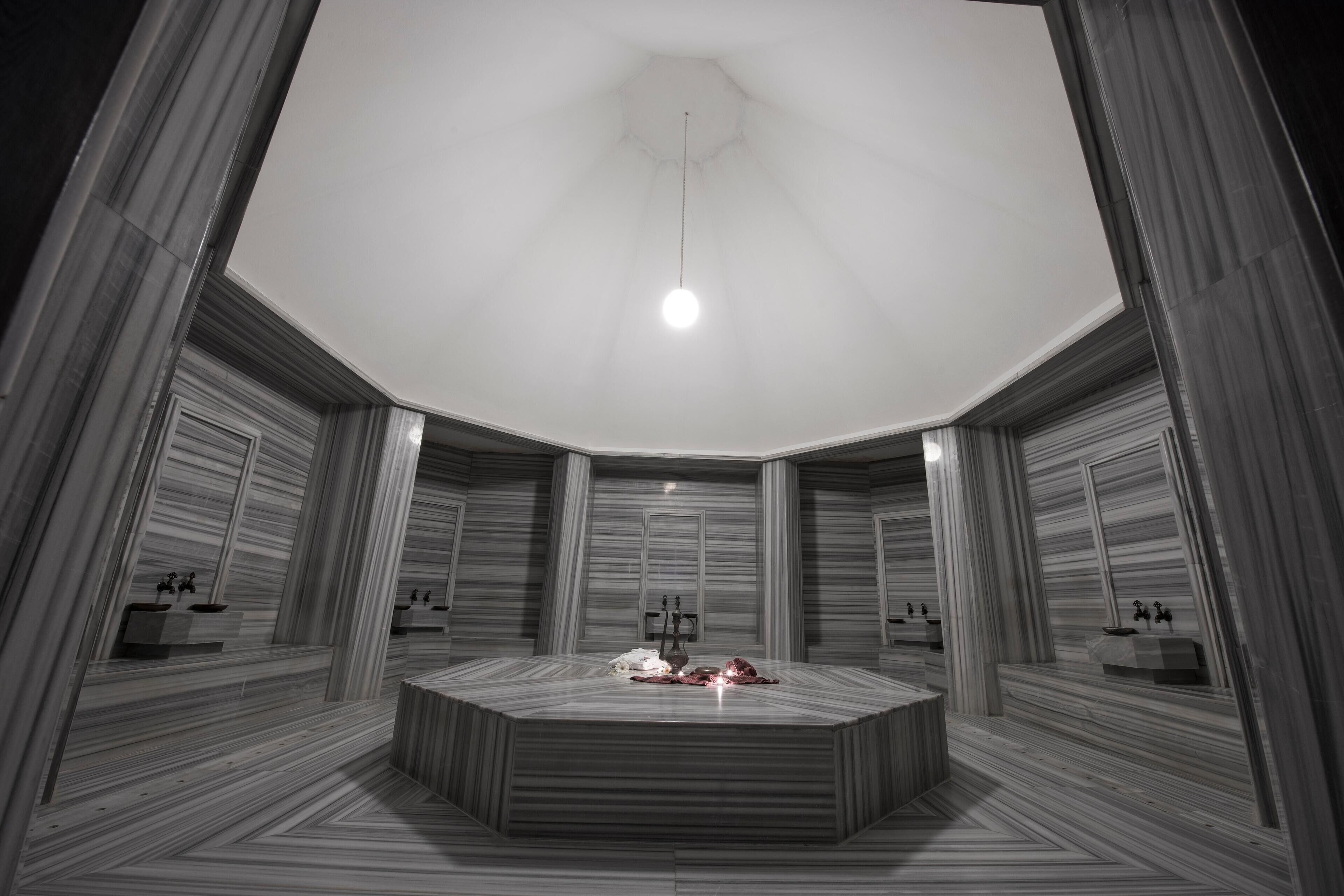 A circular room with a central table, mirrored walls, and a ceiling light.
