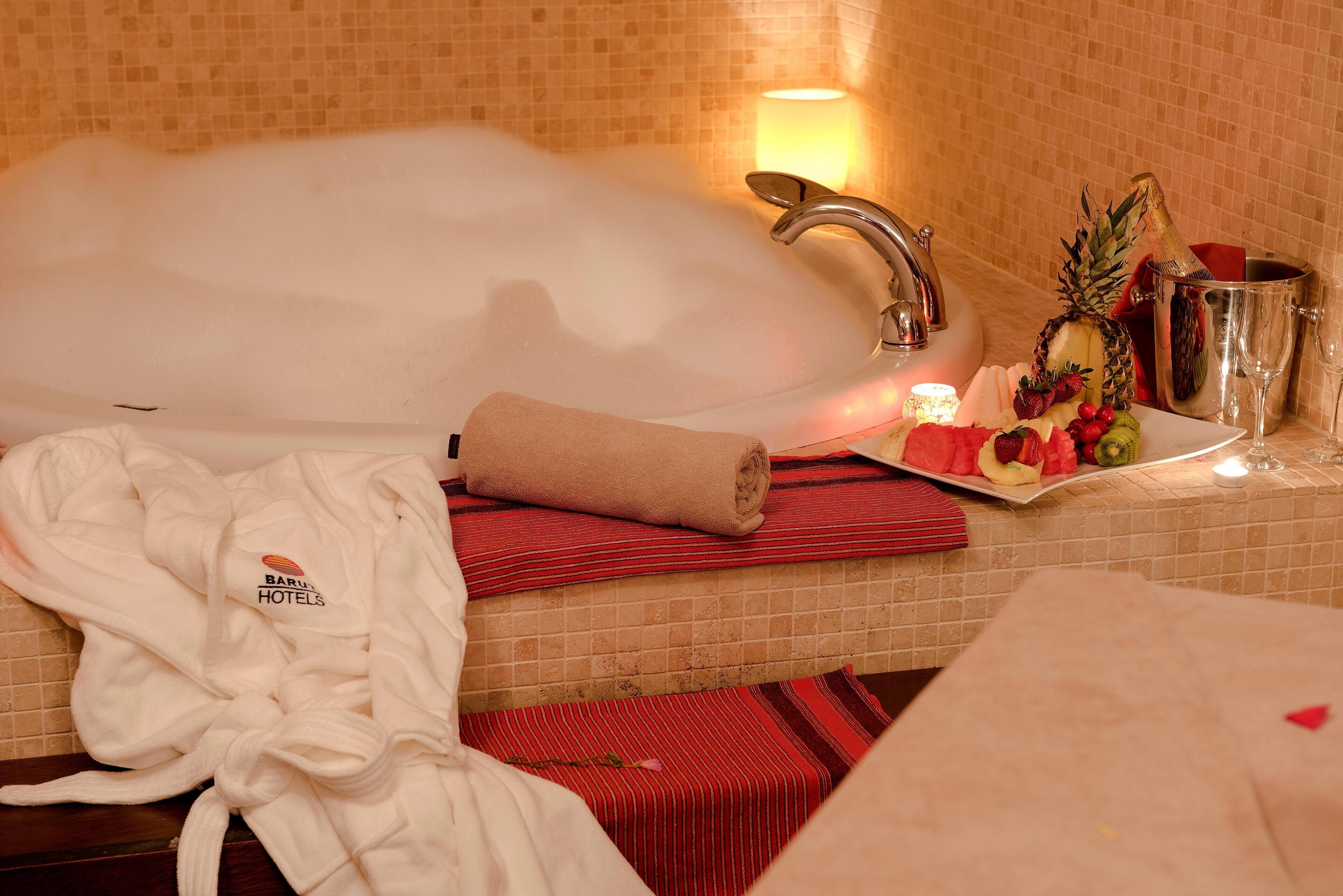 A bathroom with a bathtub, a towel, a fruit plate, and a champagne bottle.