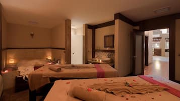 A spa room with two massage tables, each with towels and flowers. There is a sink and a mirror on the wall.