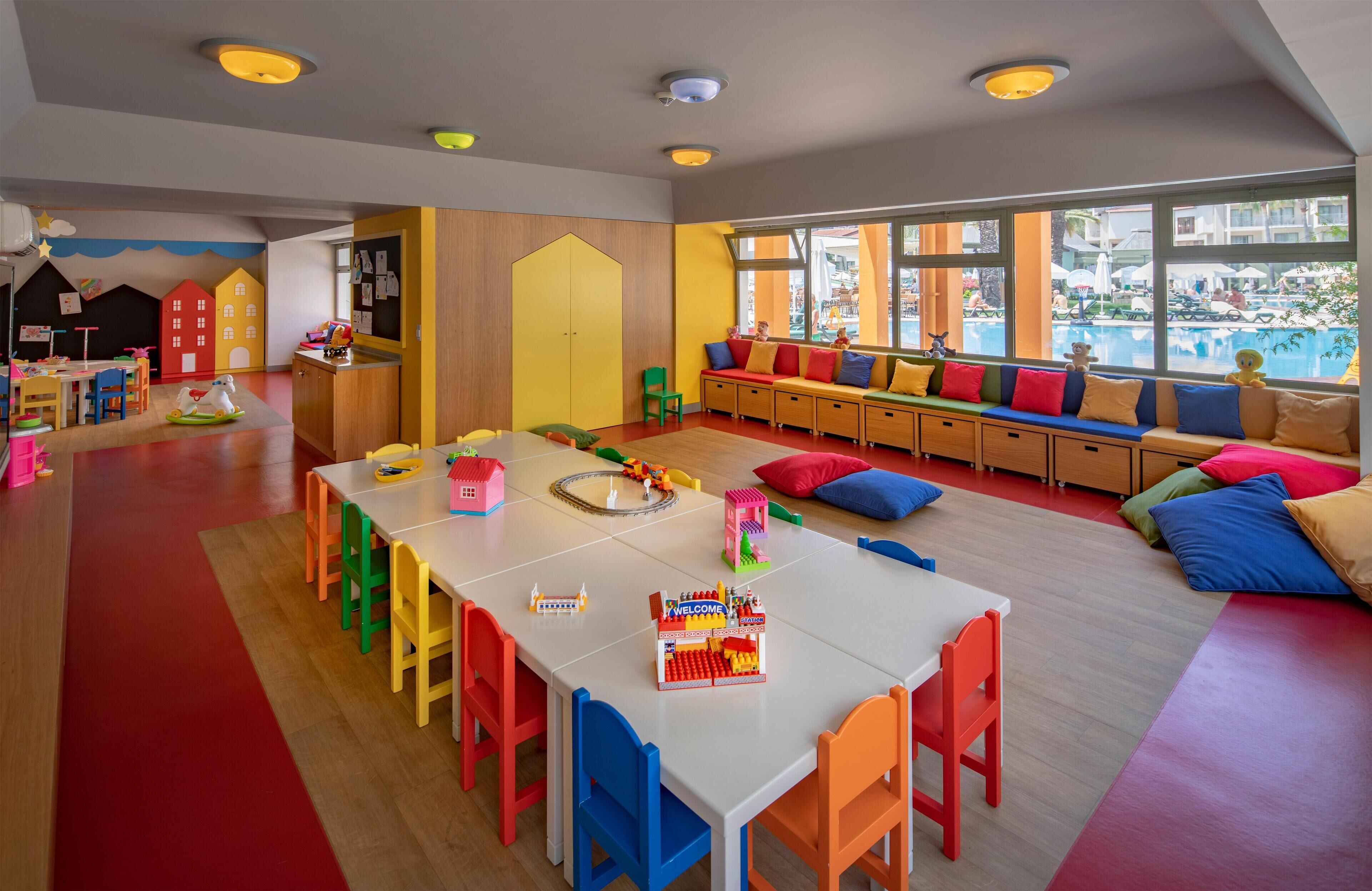 A brightly colored children's playroom with a long table, colorful chairs, and a bench with cushions.