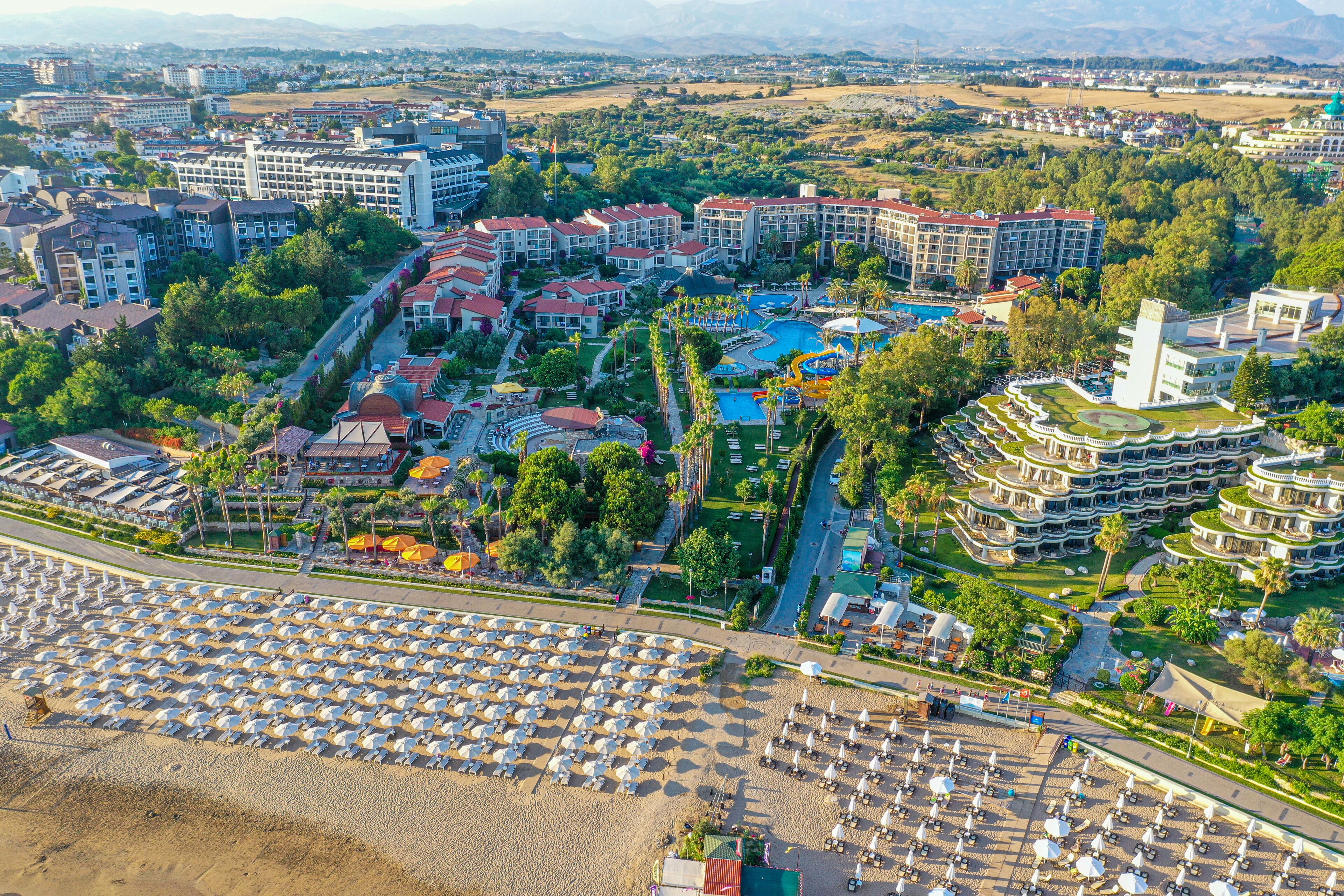 A resort with multiple buildings, a large pool area, and a beach with numerous umbrellas.