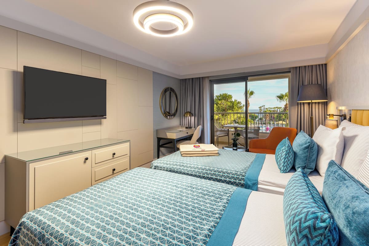 Une chambre d’hôtel avec deux lits, un bureau, une chaise, une télévision et un balcon avec vue.