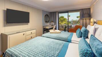 A hotel room with two beds, a desk, a chair, a TV, and a balcony with a view.
