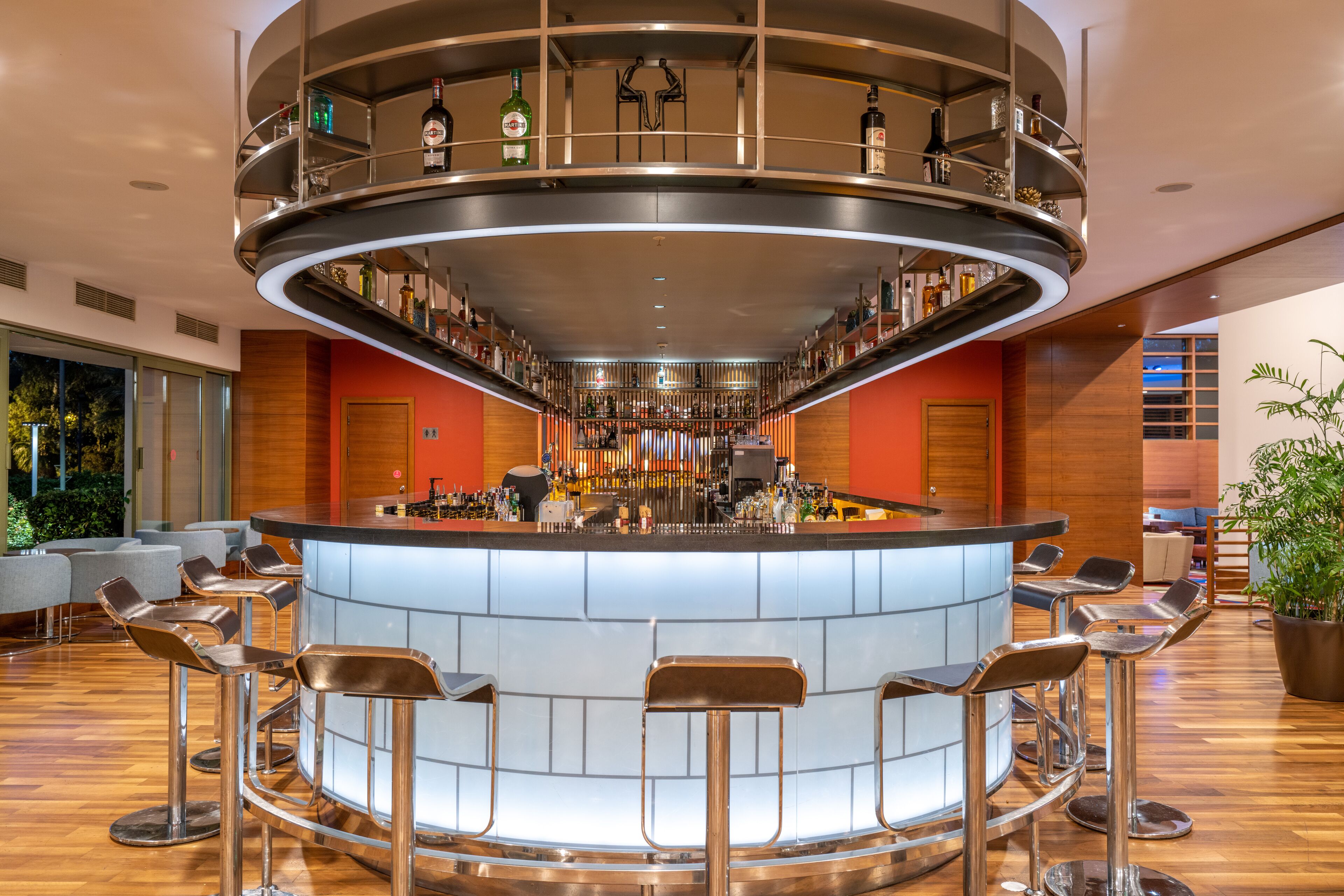 A modern bar area with a circular bar, multiple stools, and a variety of bottles on shelves.