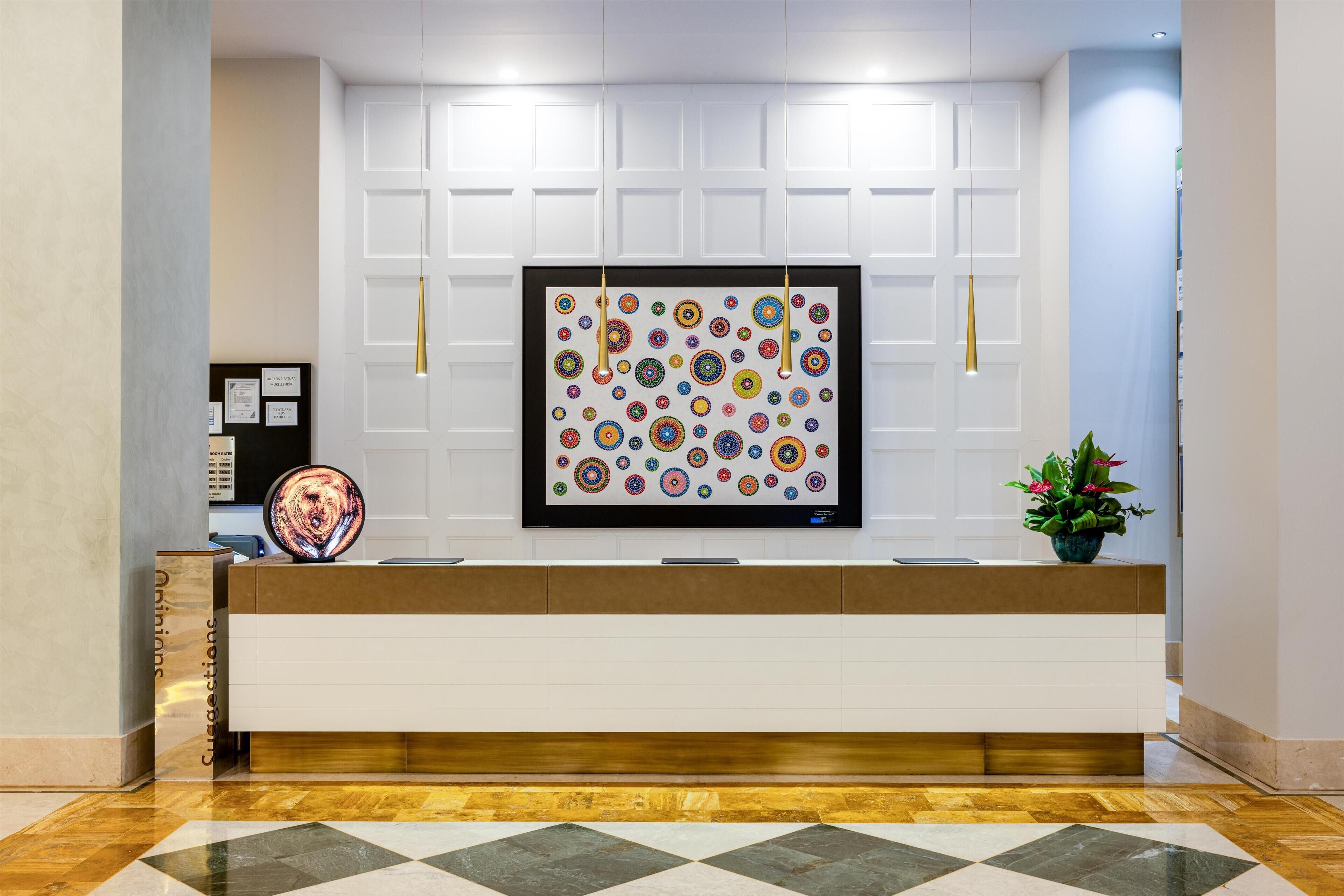 Un área de recepción con diseño moderno, que incluye un mostrador blanco, una obra de arte enmarcada en la pared y una planta en maceta.