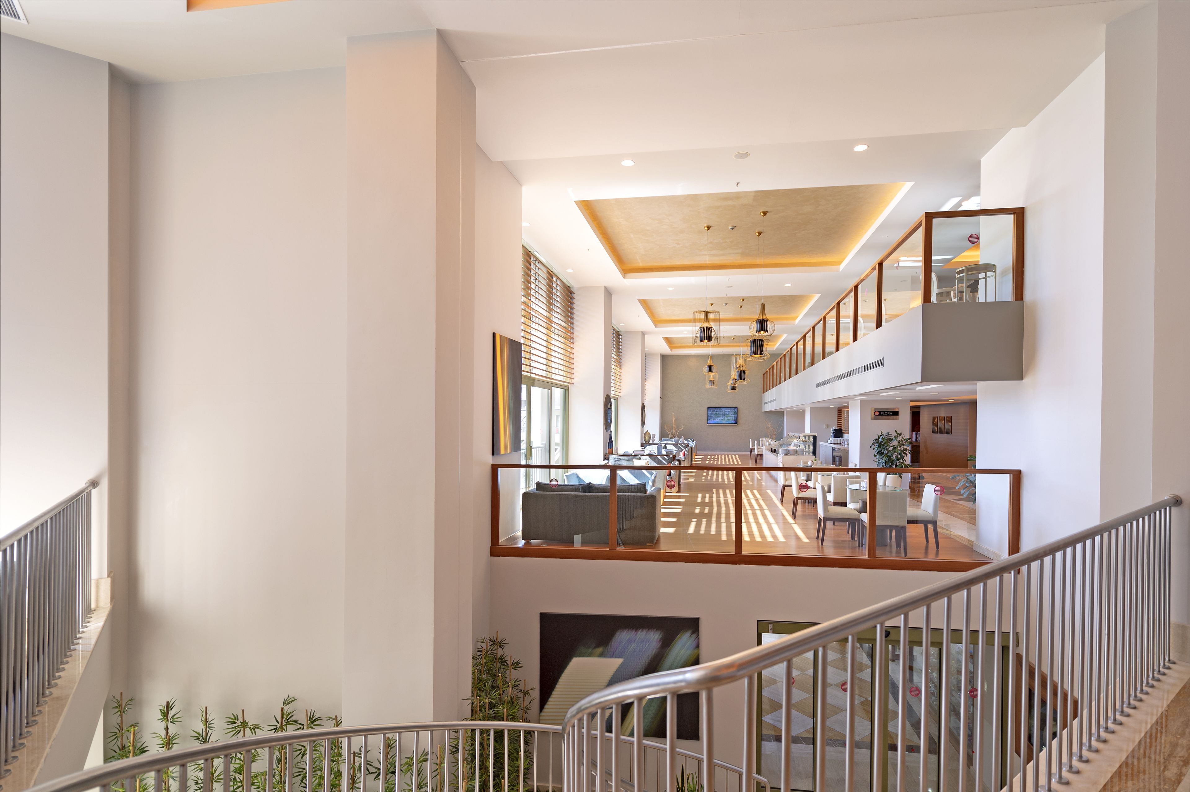 A spacious hotel lobby with a high ceiling, a central staircase, and a seating area with tables and chairs.