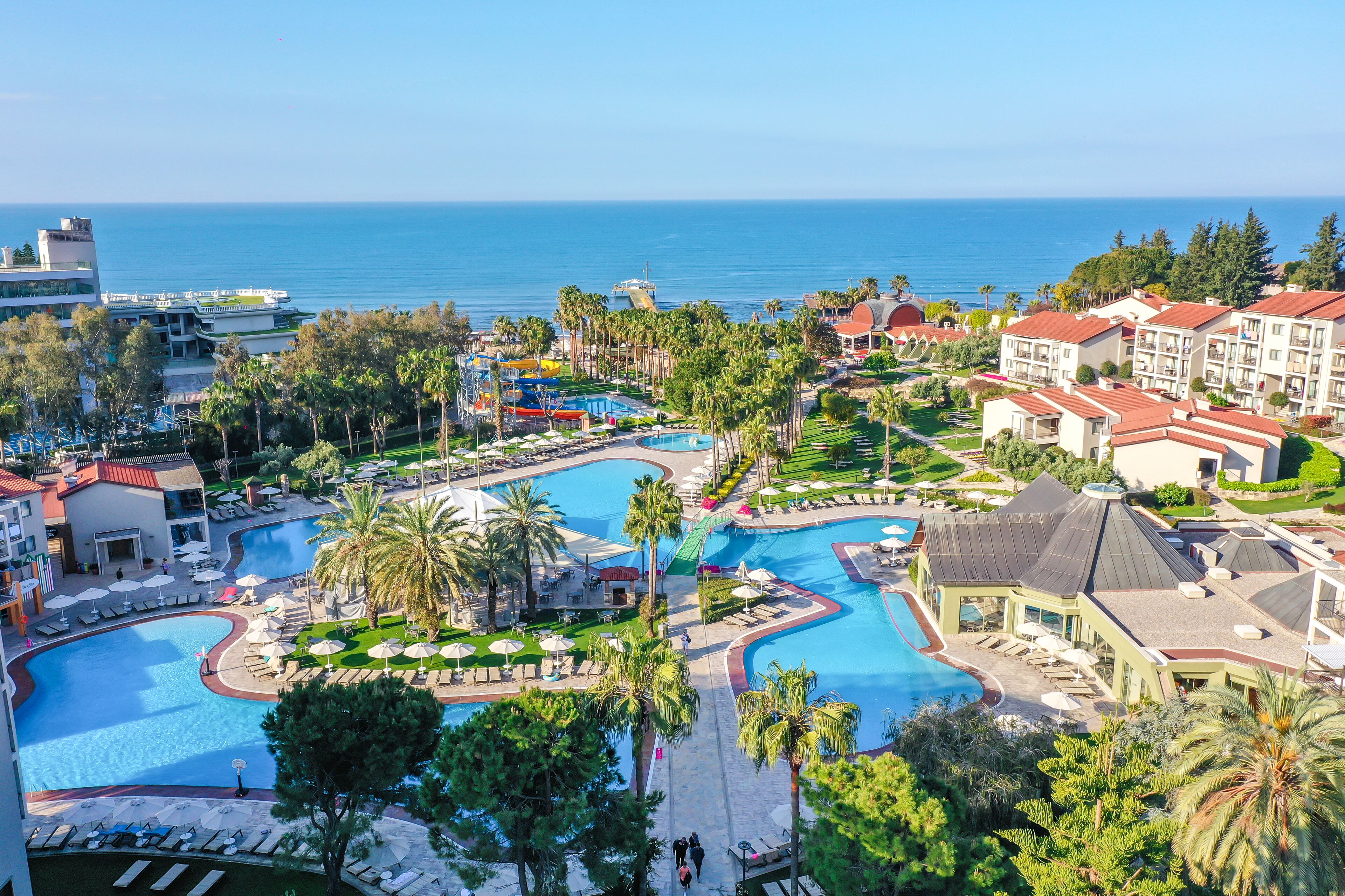 Un resort con una gran piscina, palmeras y vista al mar.