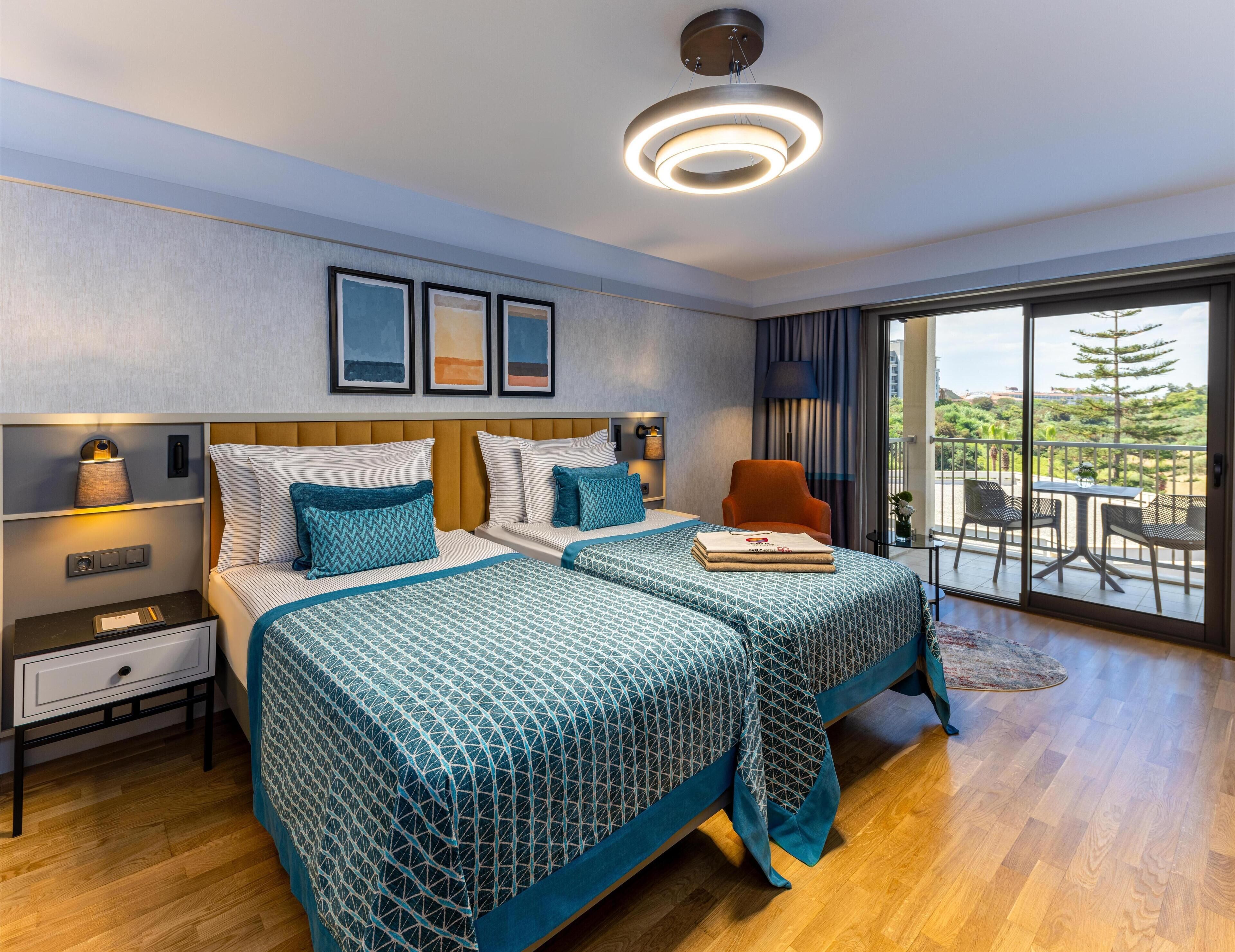Een hotelkamer met twee bedden, een nachtkastje, een lamp, een stoel en een balkon met uitzicht.