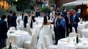 A wedding reception in an outdoor courtyard with round tables and chairs, a large brick building with a tower, and a staircase leading to an entrance. - Relais del Castello di Oviglio (Oviglio)