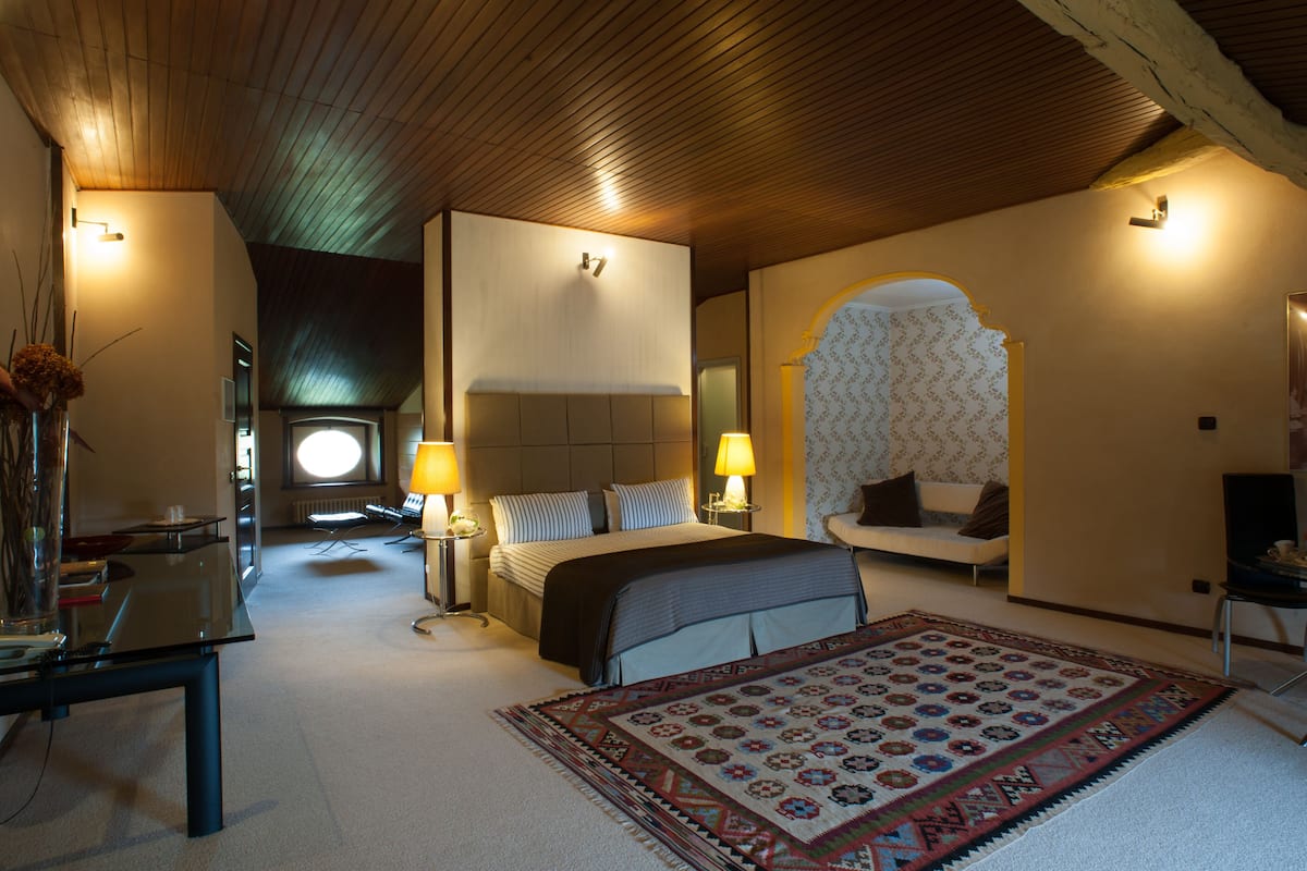 A modern bedroom with a large bed, bedside lamps, a sofa, and a patterned rug.