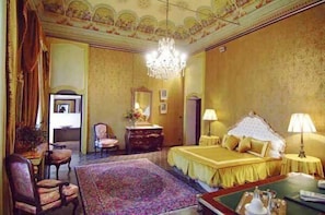 A luxurious hotel room with a large bed, a chandelier, a sitting area with a chair and table, and a decorative ceiling. - Relais del Castello di Oviglio (Oviglio)