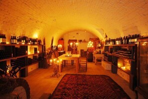 An underground wine cellar with shelves of wine bottles, a dining area with a table and chairs, and a patterned rug on the floor. - Relais del Castello di Oviglio (Oviglio)