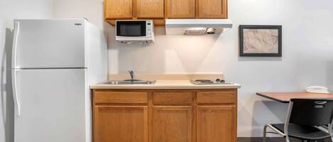 A compact kitchen with wooden cabinets, a built-in microwave, a refrigerator, and a small dining area with a chair and table.