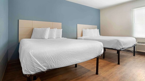 A hotel room with two beds, wooden flooring, and a window with blinds. - Extended Stay America Select Suites - Pensacola - Northwest (Pensacola)