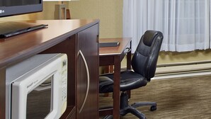 A hotel room with a wooden desk, a black office chair, a microwave, and a television.