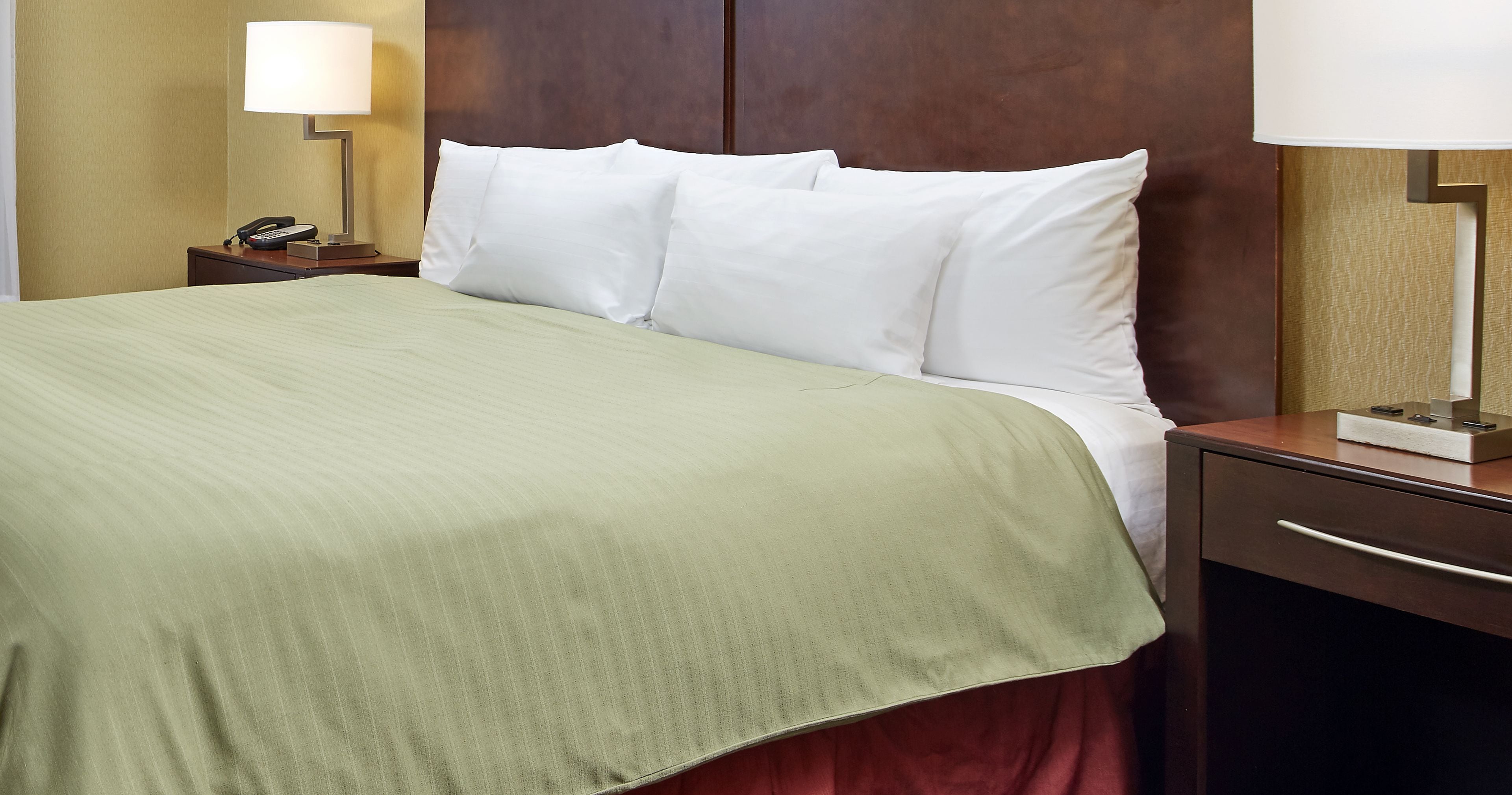 Ein Hotelzimmer mit Bett, Nachttisch mit Lampe und Schreibtisch mit Telefon.