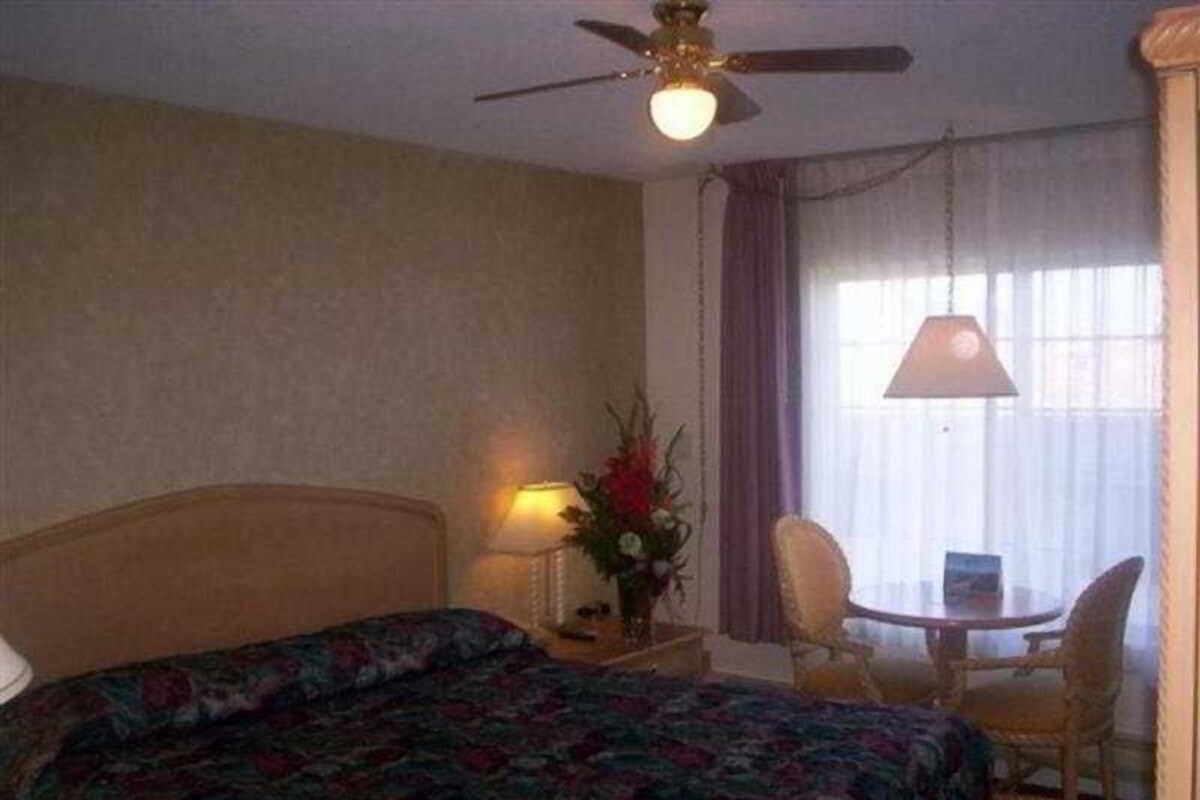 A hotel room with a bed, a nightstand with a lamp, a chair, and a table.