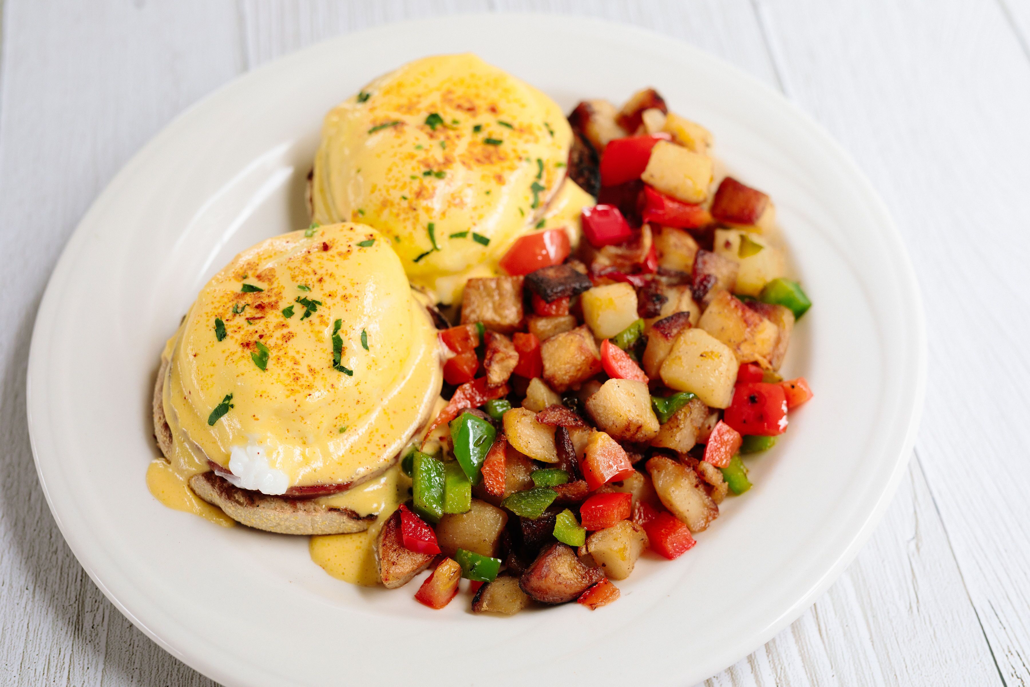 A plate with eggs benedict and a side of diced vegetables.