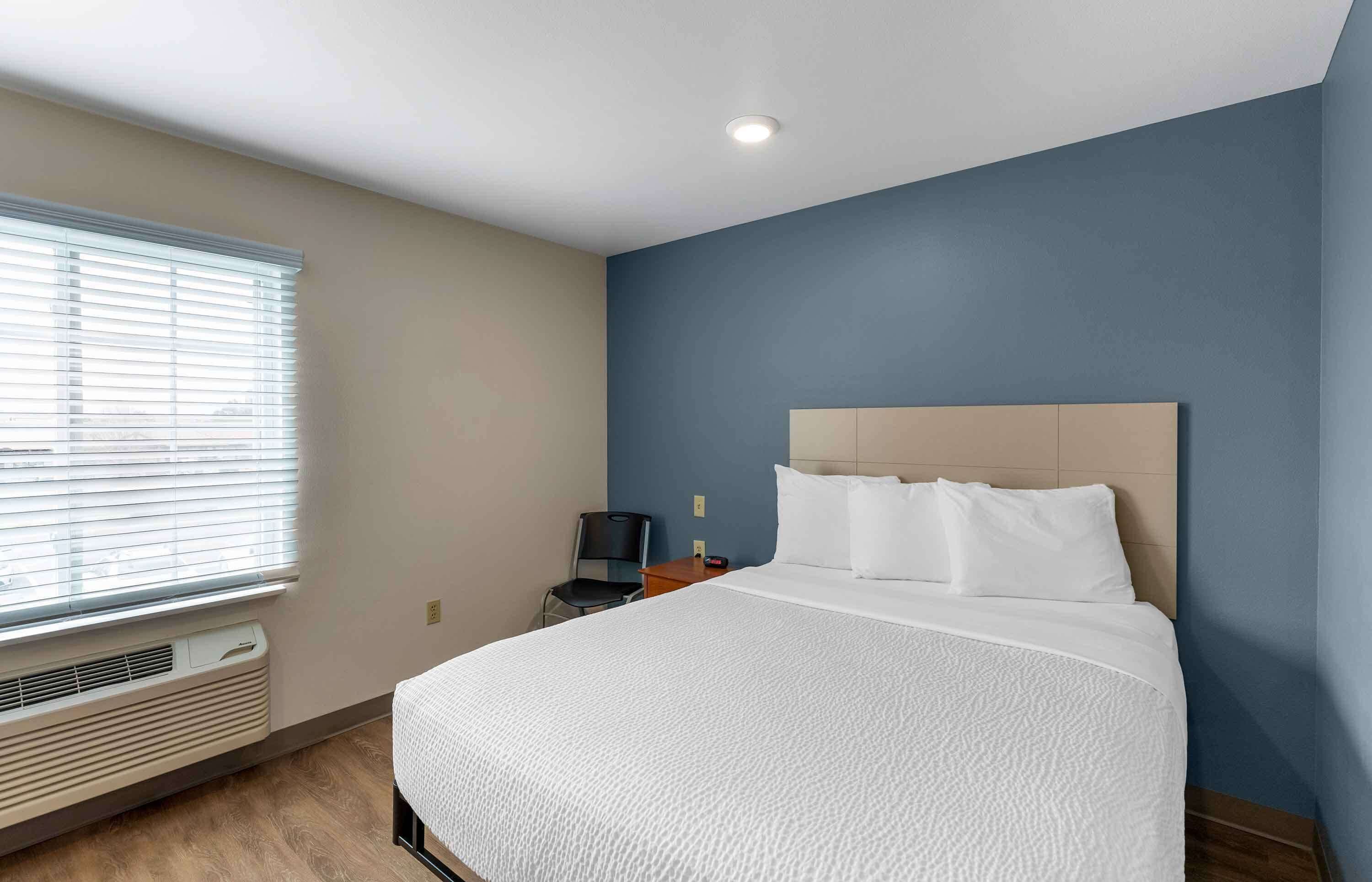 A hotel room with a large bed, a chair, a desk, and a window with blinds.