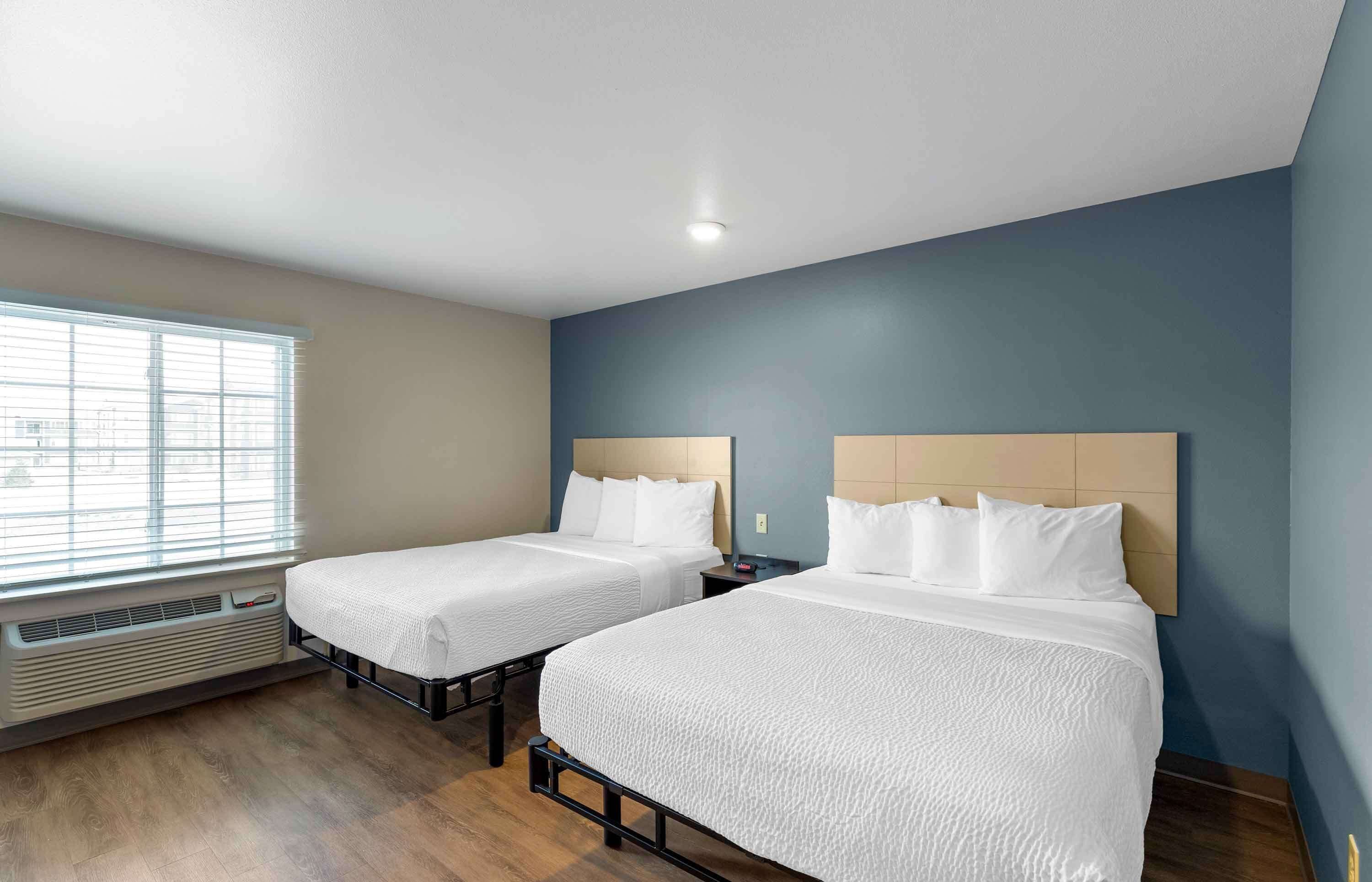 A hotel room with two beds, a window with blinds, a heater, and a ceiling light.