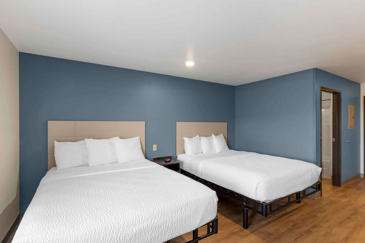 A room with two beds, wooden flooring, and a blue wall.