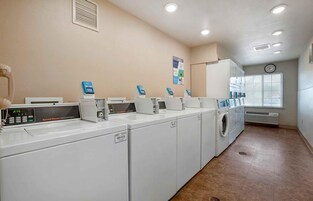 A laundry facility with multiple washing machines and dryers, a clock, and a poster on the wall.