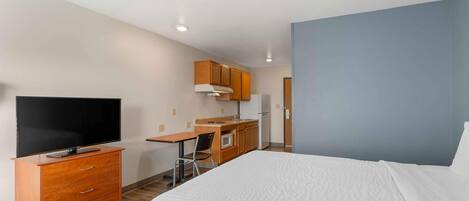 A hotel room with a bed, a TV, a kitchenette, and a desk.