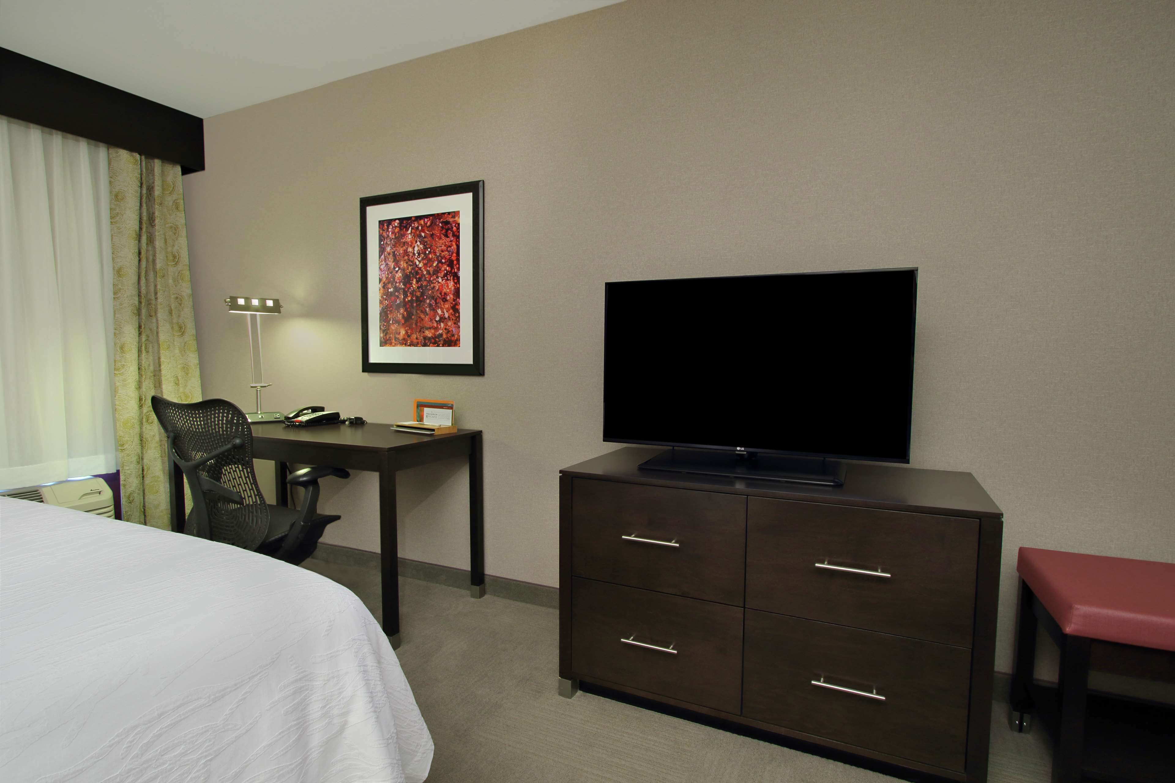 Una habitación de hotel con cama, escritorio con silla, televisor, cómoda y un banco.